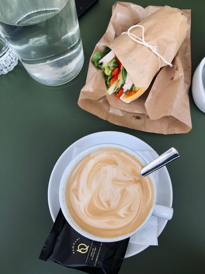 A savory latte paired with a fresh vegetable sandwich on a green table.