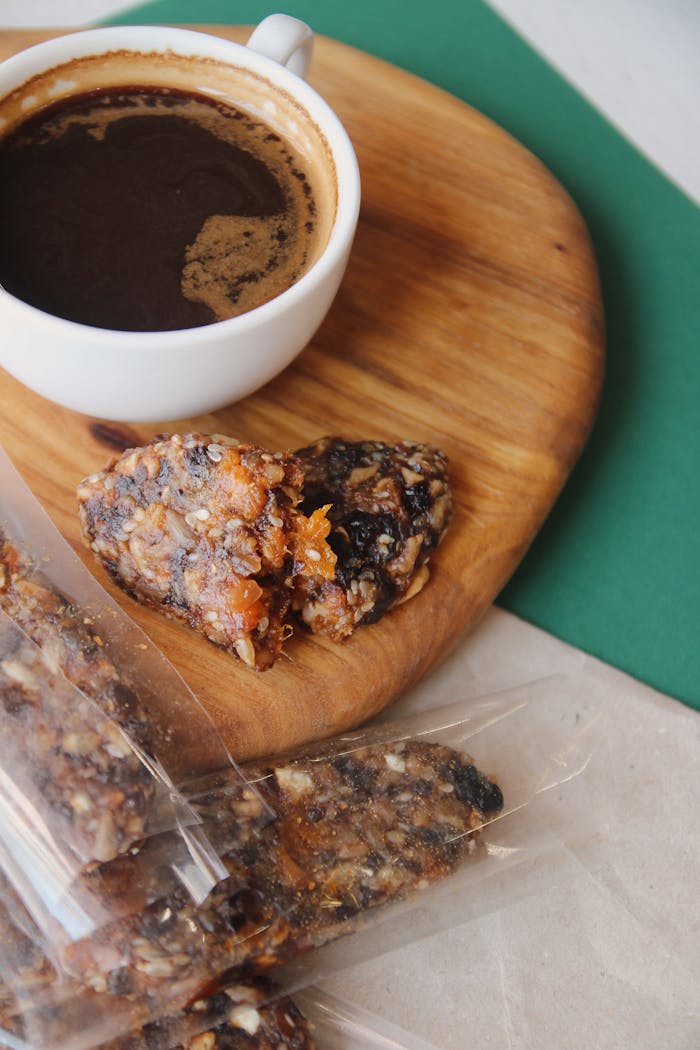 A rich black coffee with a nutty, fruity snack on a wooden board.